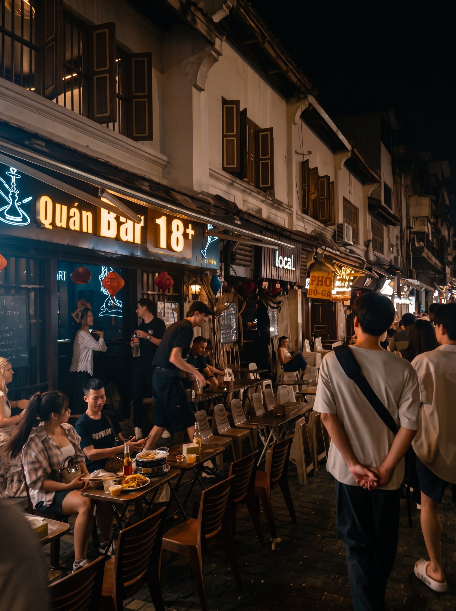People drinking at small tables under neon bar signs on Hanoi's beer street at night