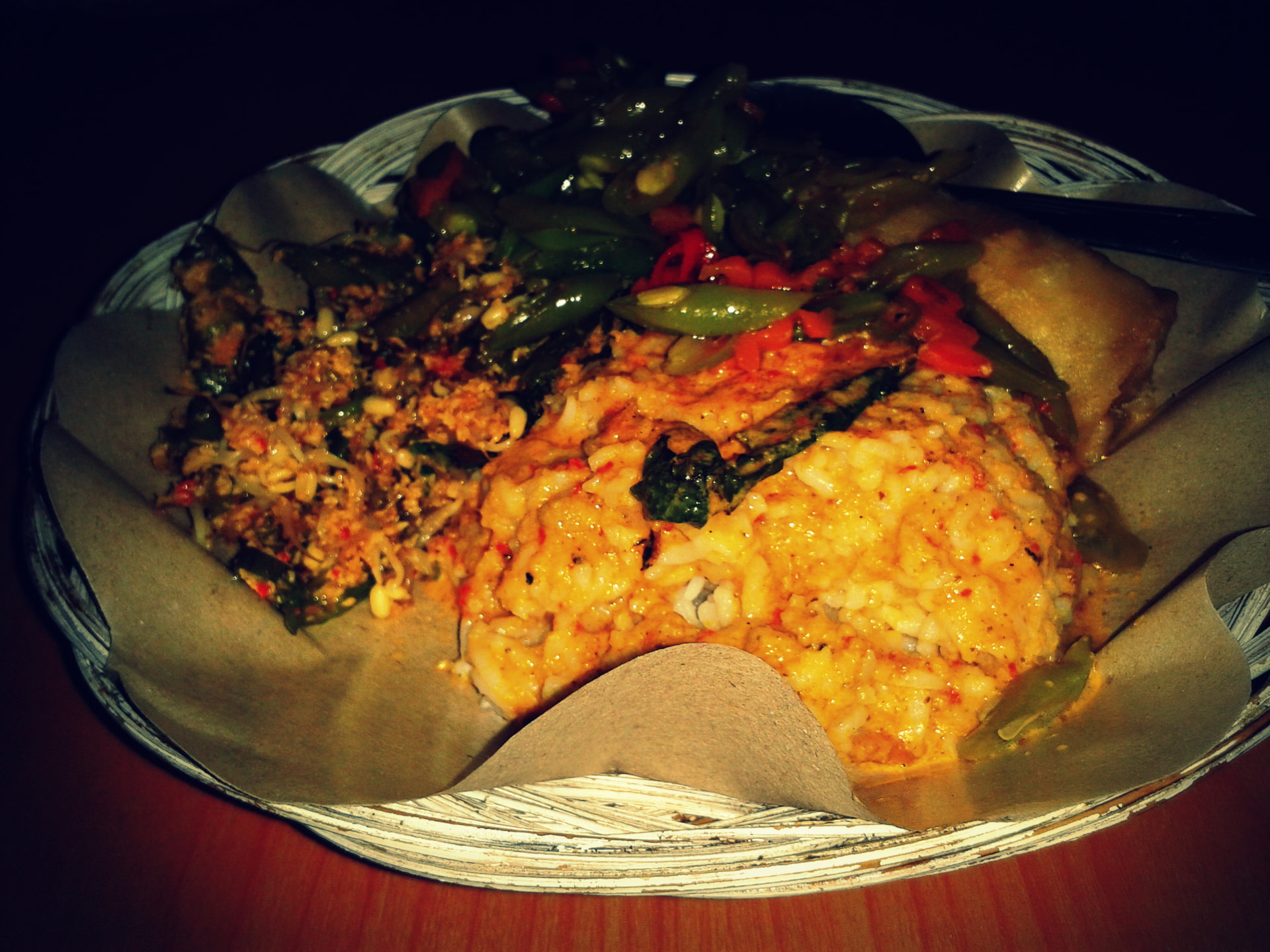 A woven basket plate of nasi campur with rice, beans, chilli and tempeh at a Bali night market