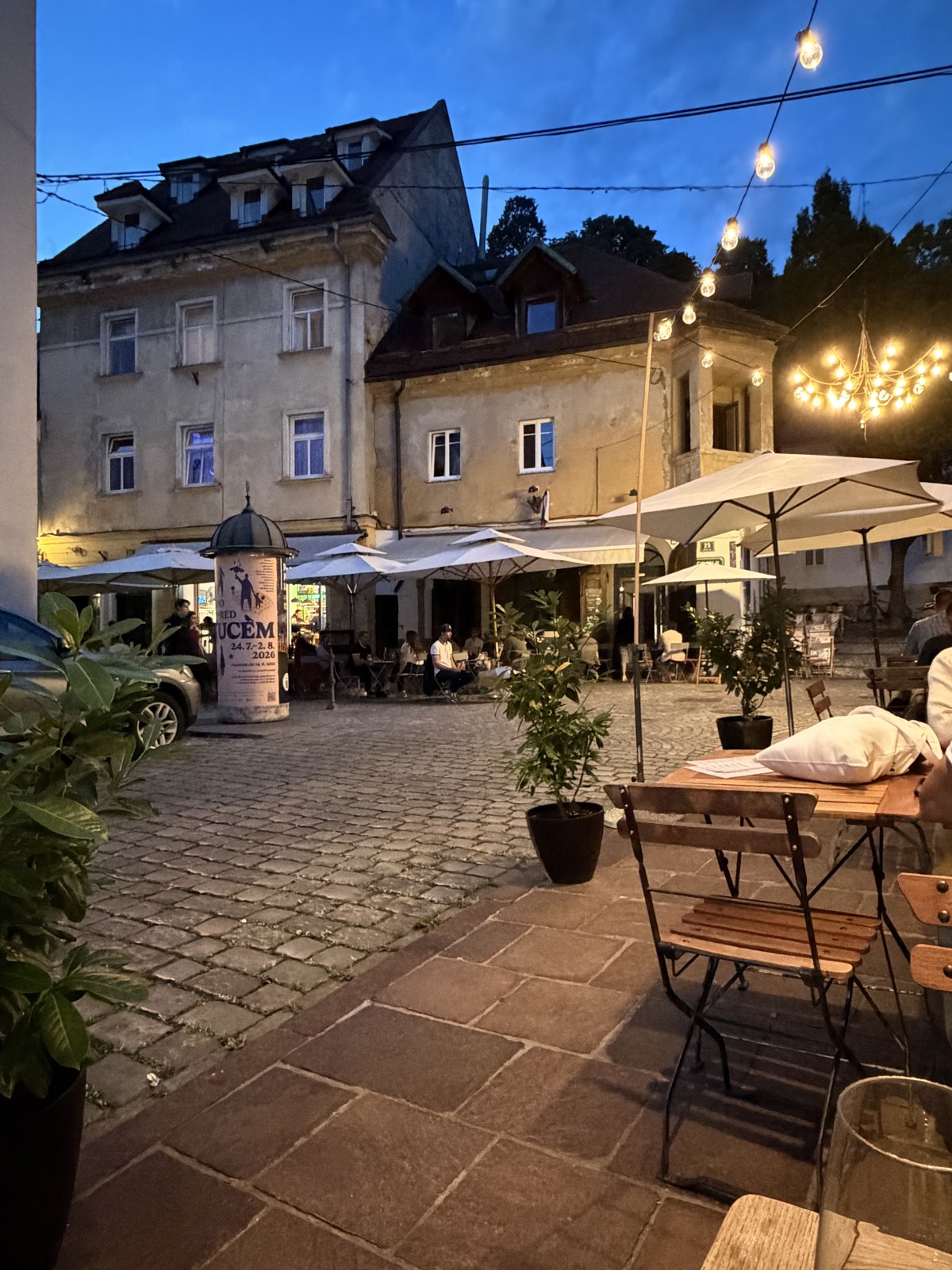 An outdoor café terrace in Ljubljana at dusk with string lights and umbrellas