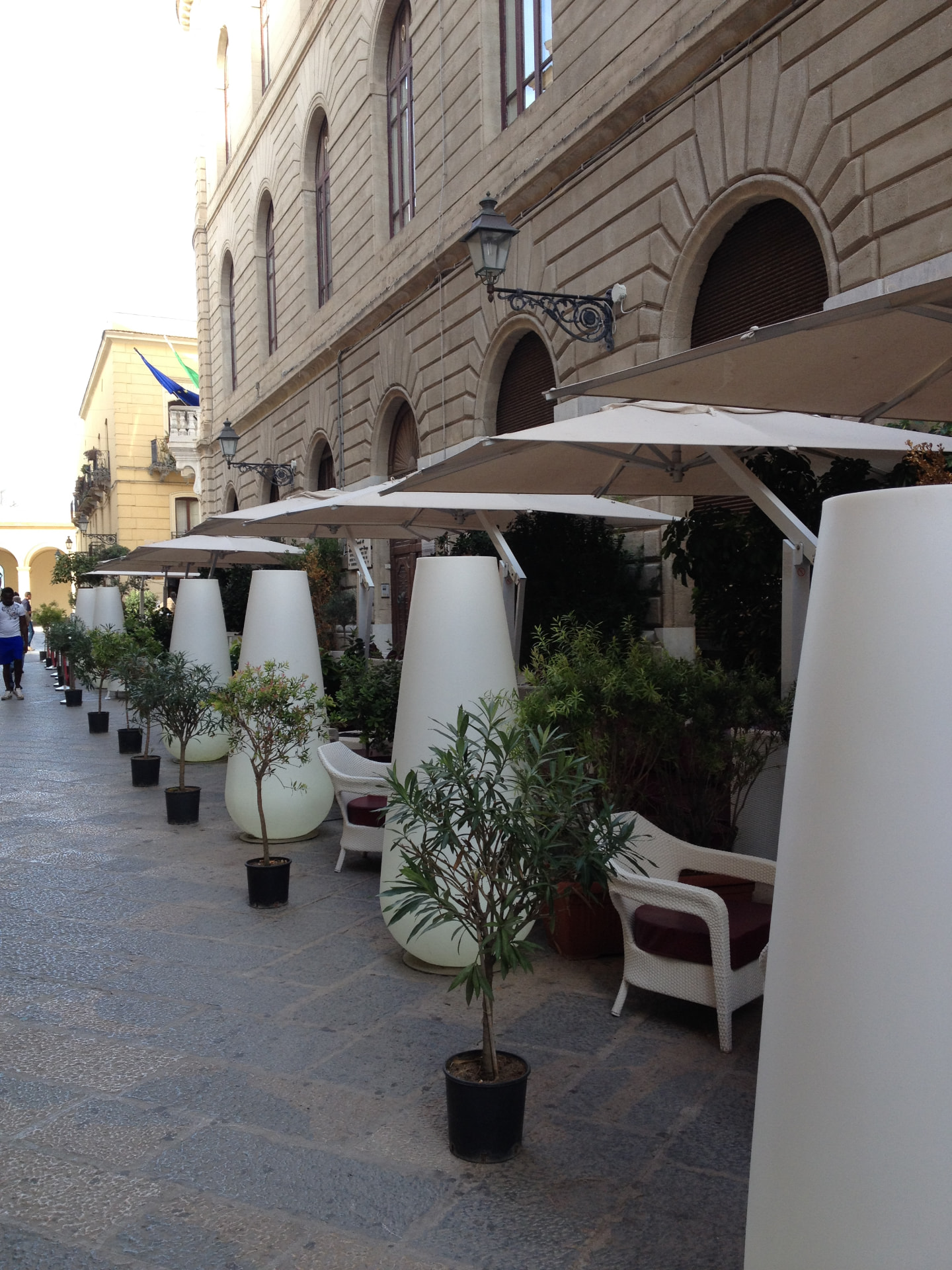 White umbrellas and potted olive trees outside a historic building in Trapani
