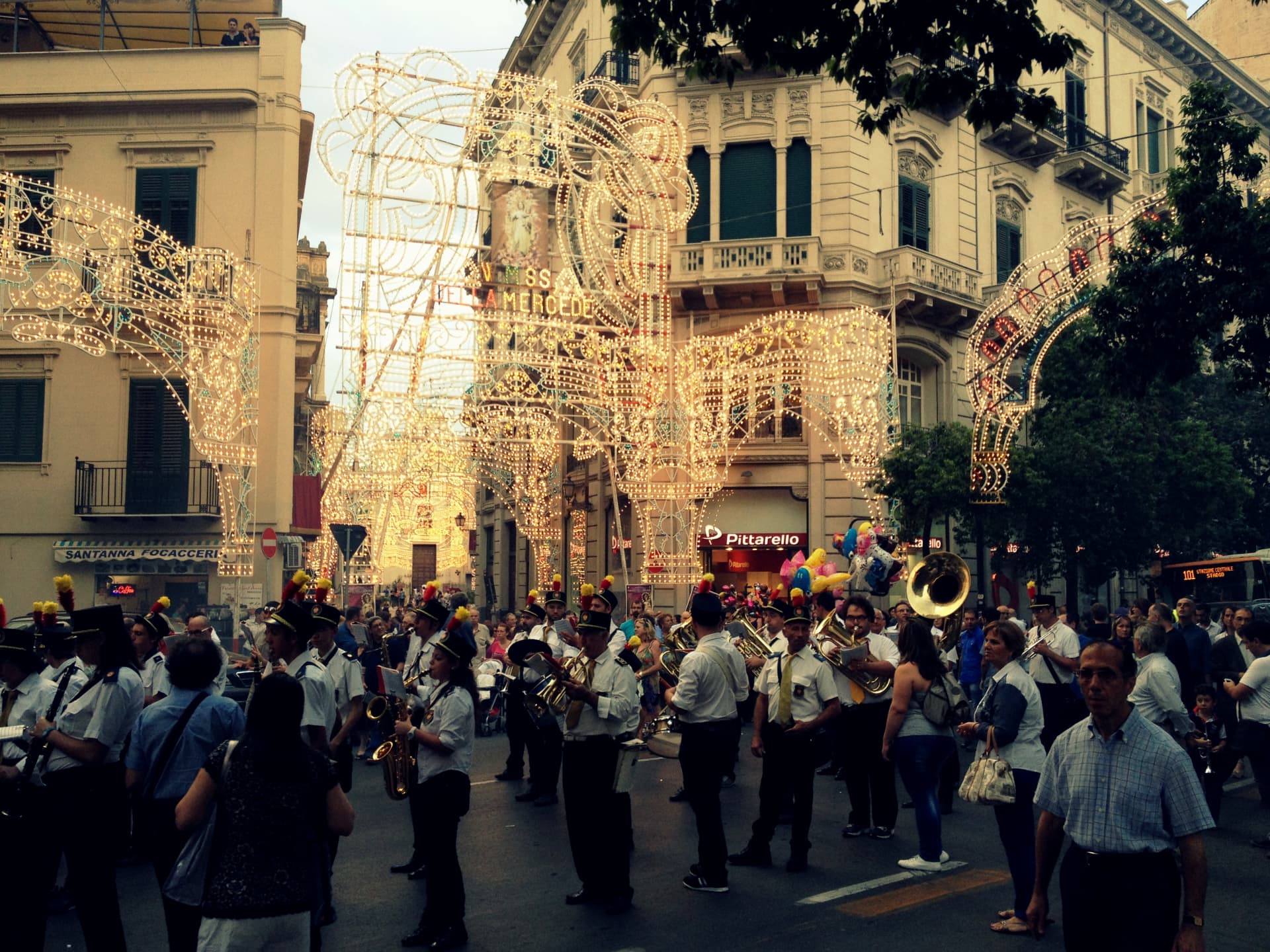 A marching band playing in a Palermo street under huge illuminated light arches