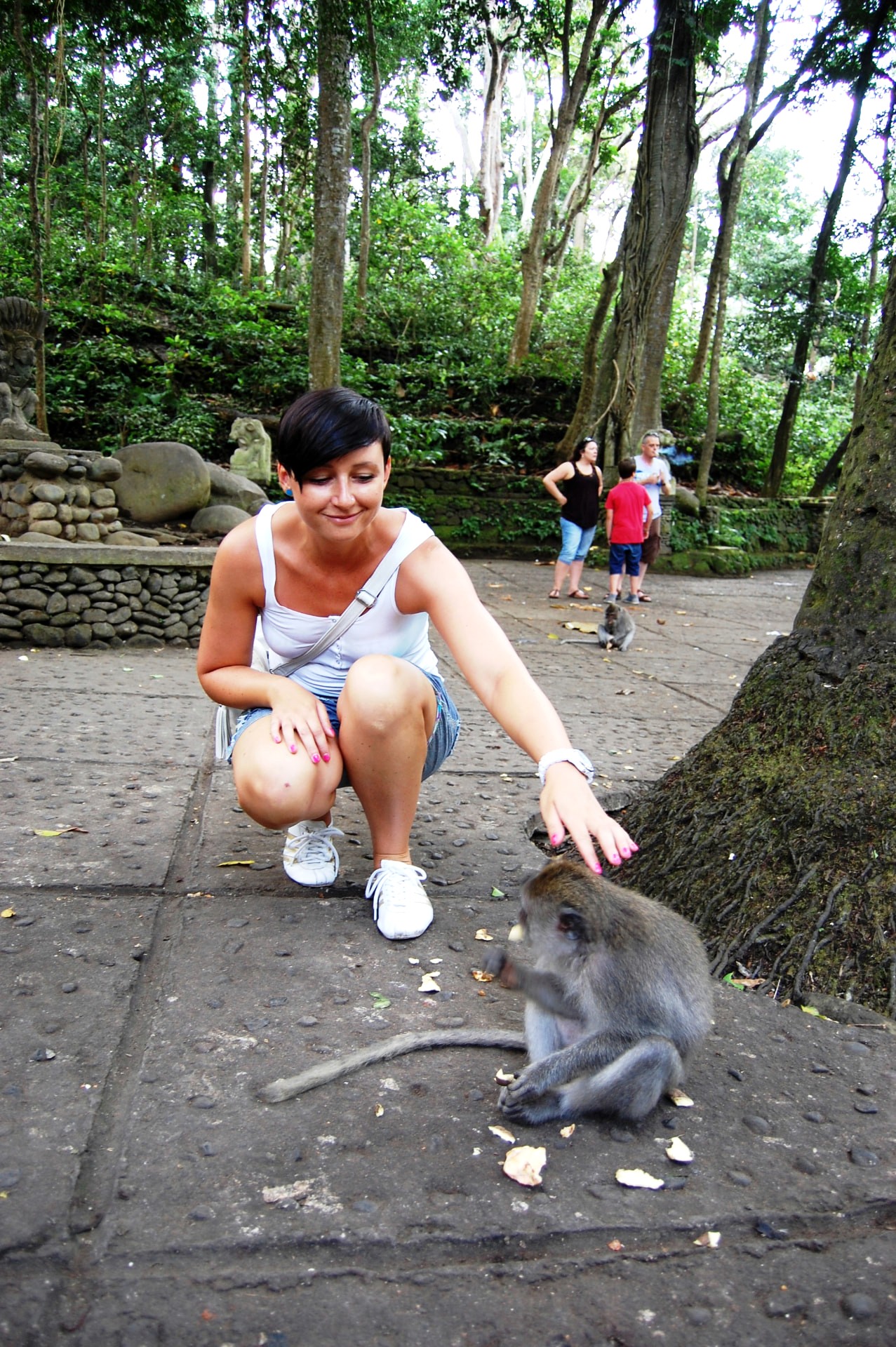 A traveller crouching to greet a macaque in the Ubud Monkey Forest