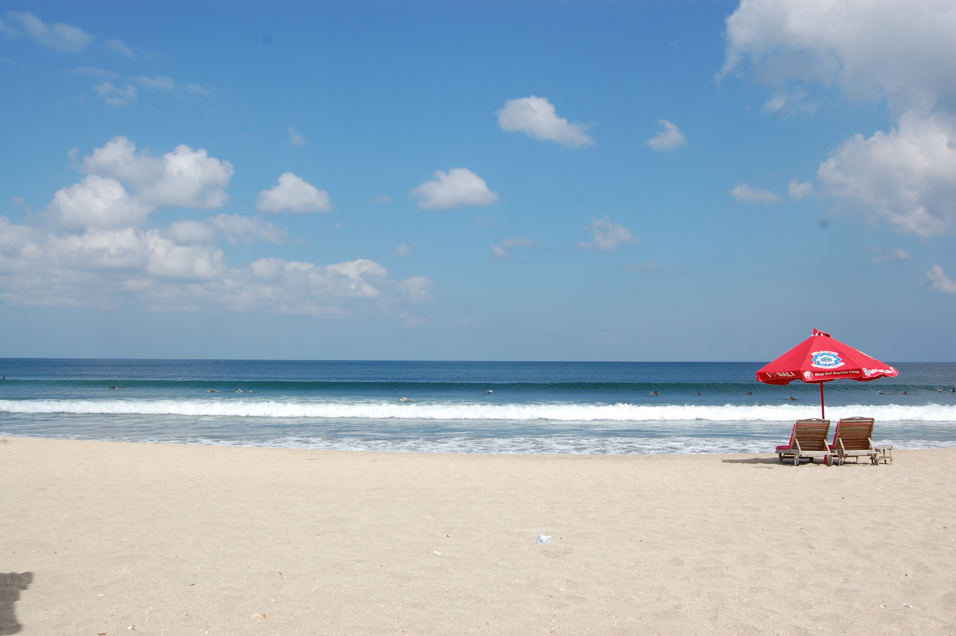 A quiet Kuta Beach in the morning with a red parasol, sun loungers and surfers waiting beyond the break