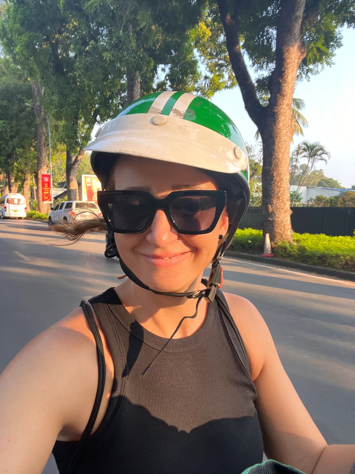 Selfie in a borrowed helmet on the back of a motorbike on a tree-lined Hanoi street