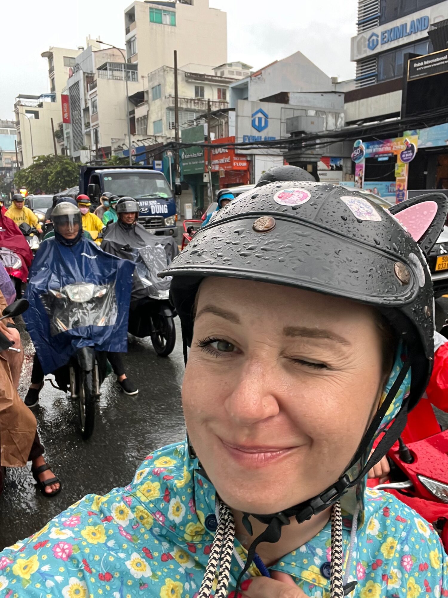 Andreja wearing a cat-ear helmet and flowery raincoat in Saigon scooter traffic