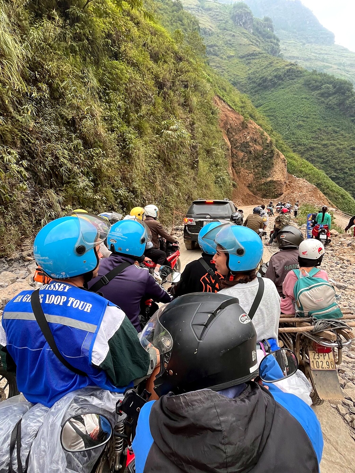 Tour riders and motorbikes waiting beside road-construction rubble