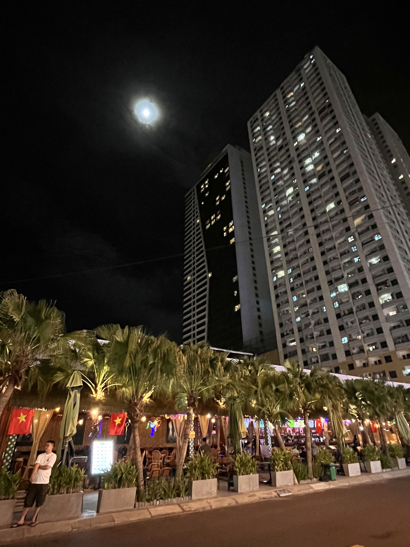 Full moon over Da Nang's tower blocks and a palm-lined restaurant terrace lit up at night
