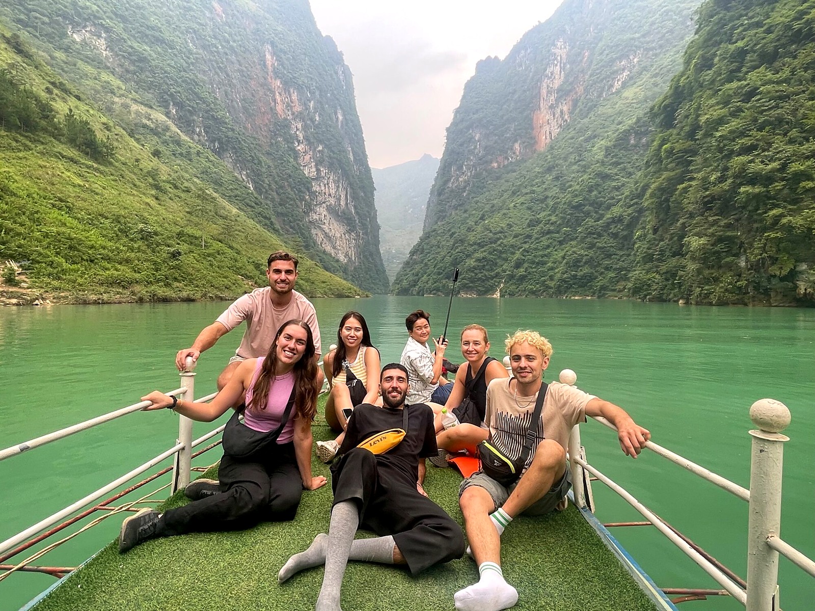 The travel group posing on a boat surrounded by green river water and steep cliffs