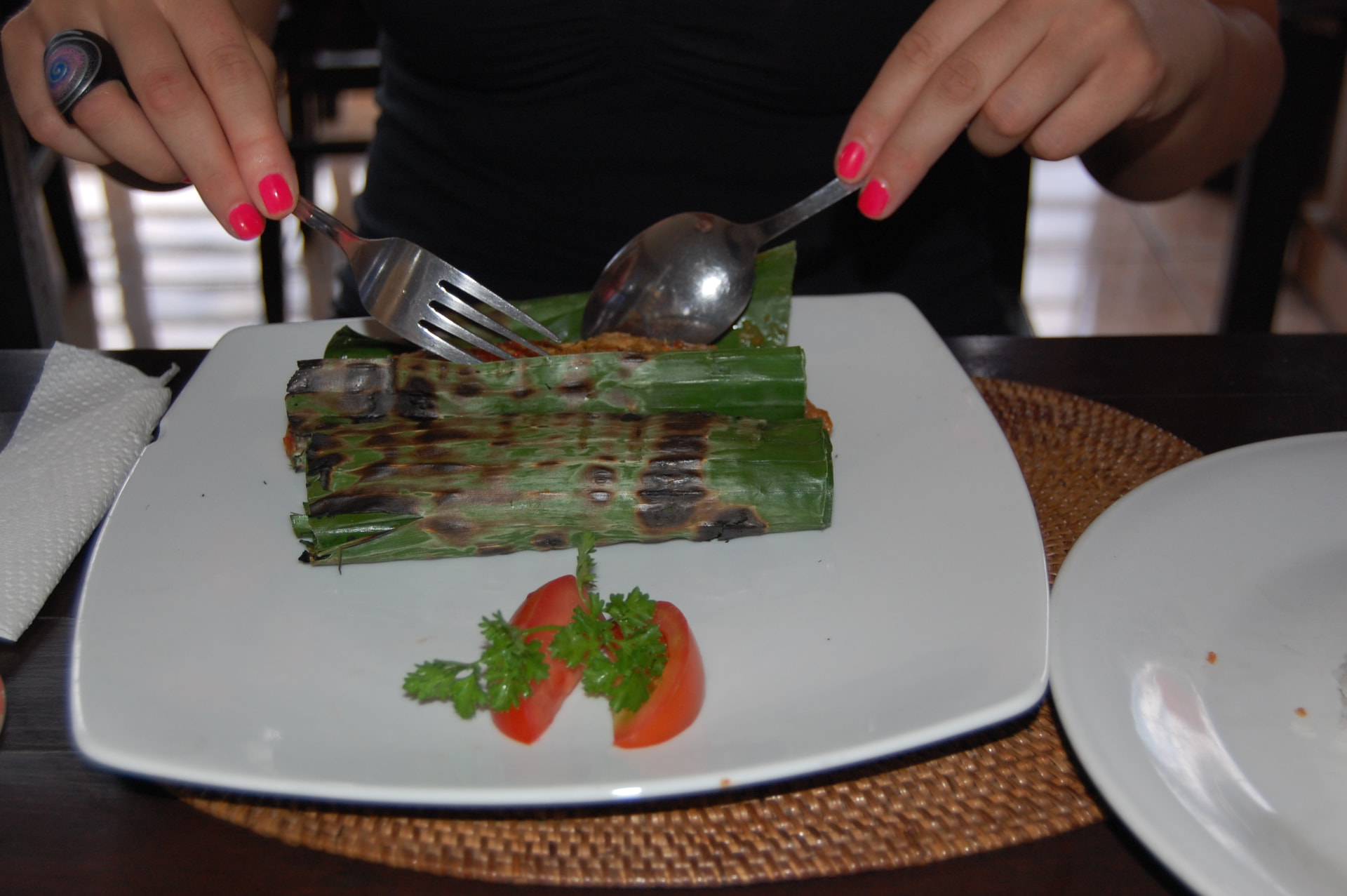 Grilled banana-leaf parcels of pepes with tomato and parsley on a white plate in Bali