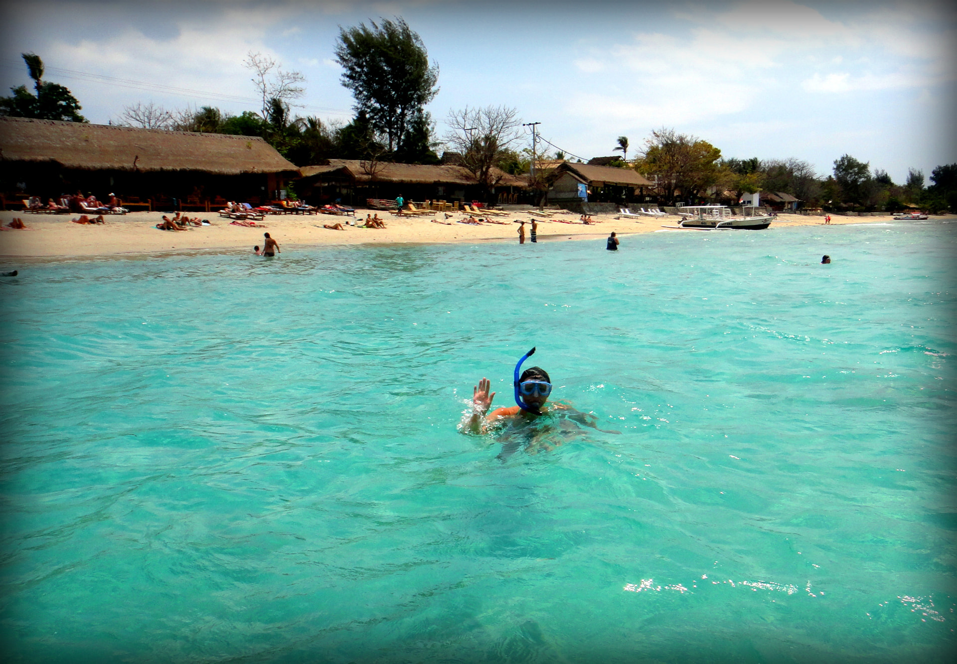 A snorkeler waving from clear turquoise shallow water off a Gili beach