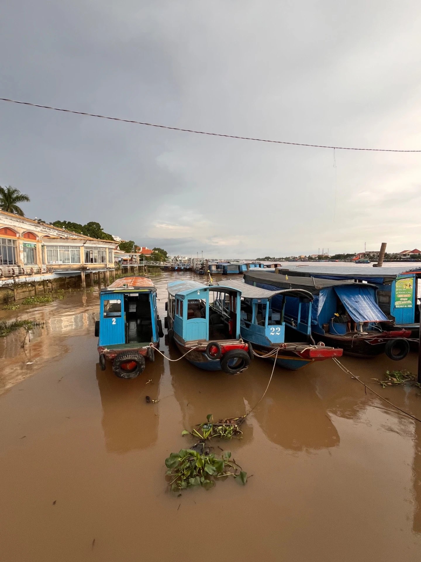 Blue wooden riverboats docked on the muddy Mekong river under a dramatic sky