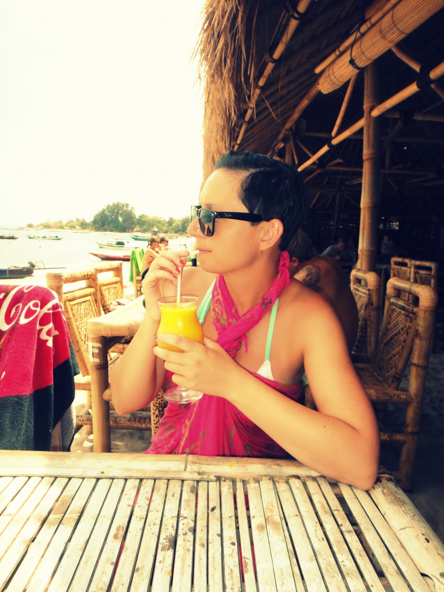 Woman in a pink sarong drinking fresh mango juice at a bamboo beach bar on Gili Meno