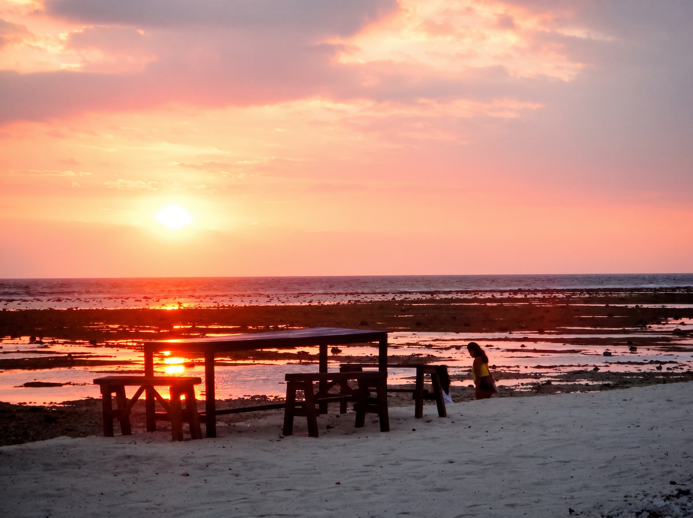 Pink and orange sunset over the reef flats with a wooden beach table in silhouette on Gili Trawangan